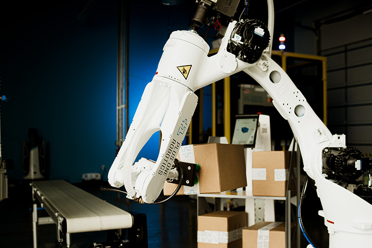 Ein Roboterarm nimmt Gegenstände auf und legt sie auf ein Förderband