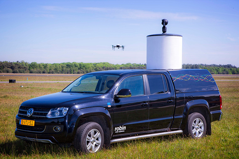 Photo of a radar on top of a vehicle and a drone flying nearby.